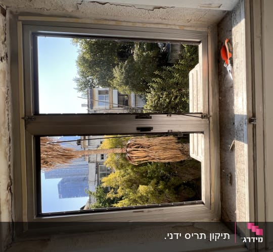 חלון עם תריסים פתוחים וכלי עבודה על אדן החלון